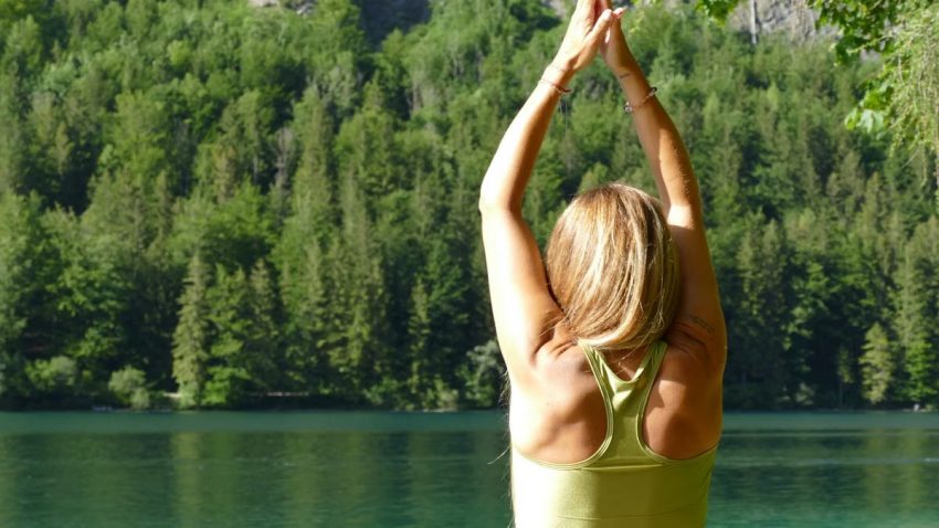 Back view of a woman meditating in a yoga pose by a serene lake in Ebensee, Austria.